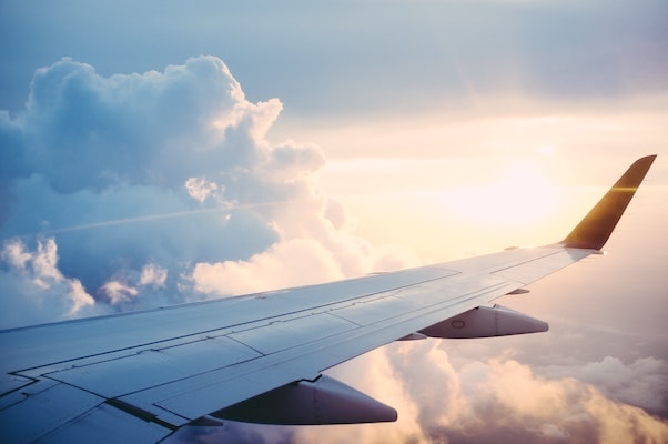 A view of a plane's wing, clouds and the sun from the plane's window